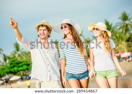 Group of happy young people having a great time on the beach on beautiful summer sunset with palms on background