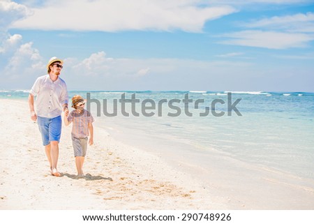 Happy hipster father and his small son having great quality family time enjoying white sand and the ocean on beautiful sunny day on summer holidays