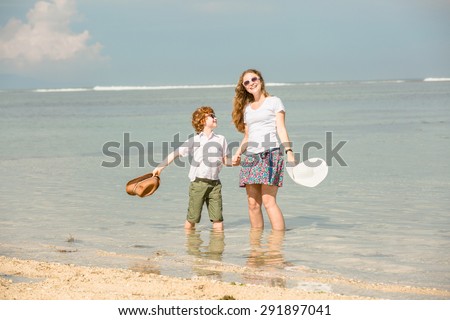 Mother and red haired son having family time on holidays waving with hats on  the beach. Travel, holiday, vacation concept