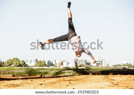 Young fit sporty woman doing simple acrobatics exercise routine in autumn park with city at background
