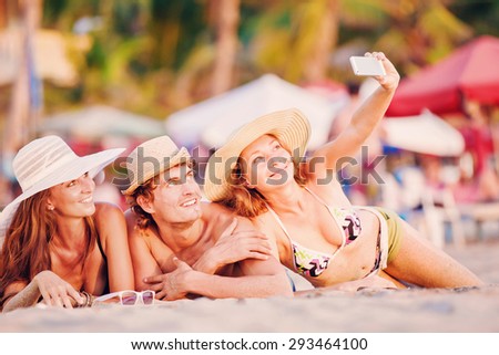Group of happy young people in bathing suits enjoying sunset on the beach and taking selfie picture, self photo during joyful holidays
