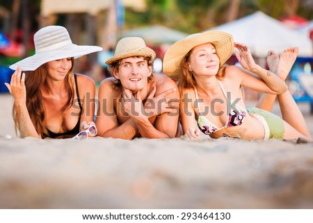 Group of happy young people in bathing suits enjoying sunset on the beach and having fun during joyful holidays