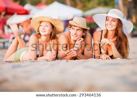 Group of happy young people in bathing suits enjoying sunset on the beach and having fun during joyful holidays