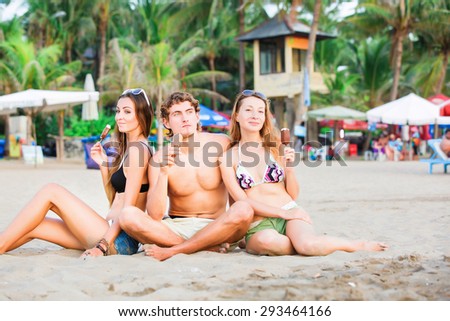 Group of happy young people in bathing suits eating ice cream on the beach and having fun