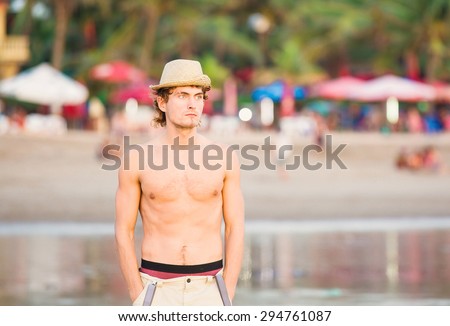 Young hot caucasian guy in a hat staying on the beach in sunset lite and thinking of eternity