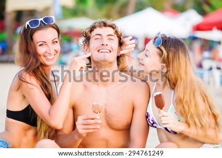 Group of happy young people in bathing suits eating ice cream on the beach and having fun