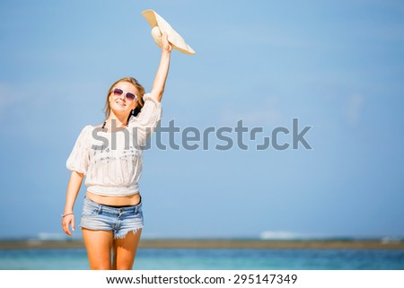Young skinny caucasian girl at the beach waving with white hat over blue sky and pure ocean water on background. Travel, vacation, holidays, paradise concept, copyspace