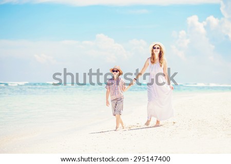 Happy mother and son walk along the white sand ocean beach having great family time on vacation on Pandawa Beach, Bali. Paradise, travel, vacation concept