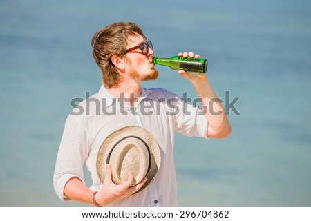 Man wearing hat and sunglasses enjoying beer in a bottle on the beach on beautiful summer holidays day