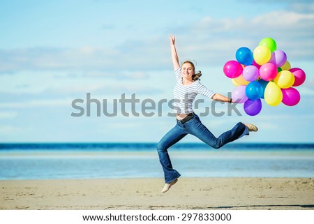 Young attractive female girl jumps on the beach holding colored balloons. Happiness, freedom, success concept