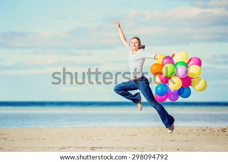 Young attractive female girl jumps on the beach holding colored balloons. Happiness, freedom, success concept