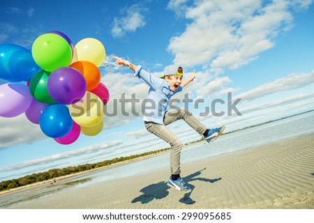 Happy boy plays with colored balloons on the beach having great holidays time on summer. Lifestyle, vacation, happiness, joy concept