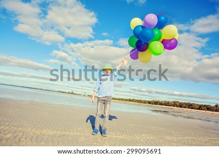 Happy boy plays with colored balloons on the beach having great holidays time on summer. Lifestyle, vacation, happiness, joy concept