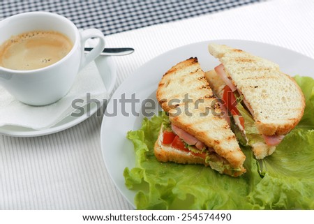 Cup of coffee and a sandwich with lettuce and tomato on a table with a checkered napkin