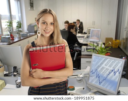 Young employee stands in the office in front of her workplace.