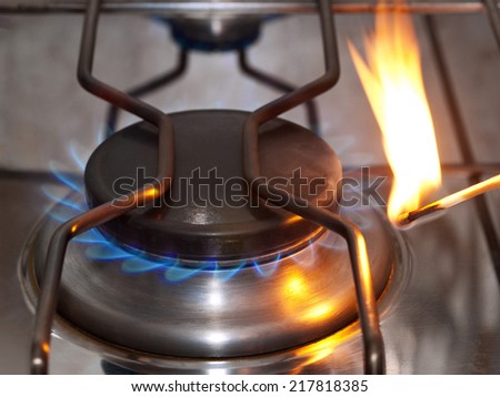 Cooking range of a gas stove is lit with a match.