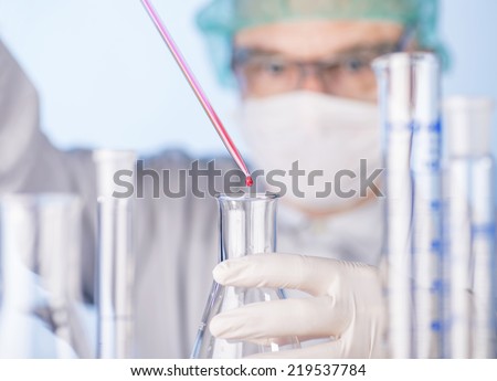Scientists with mouthguard uses pipette and flask in the laboratory.