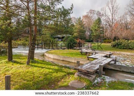 Landscape with the first snow in the autumn Japanese garden with a wooden bridge, pond and pavilion