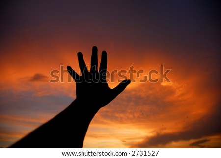 human hand trying to reach the sky at sunset