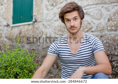 young casual man posing seated, looking at the camera, outdoors