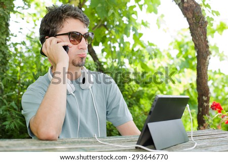young man at the phone and tablet pc with headphones, outdoor