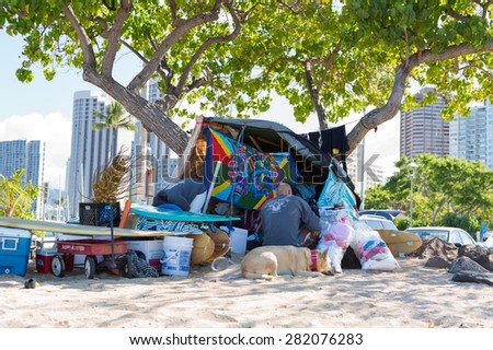 Honolulu, Hawaii, USA, May 28, 2015: Homeless man and his dog camping on a beach in Waikiki with landmark hotels in the background. The homeless problem in Hawaii affects tourists and locals.