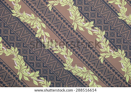 Vintage Polynesian cloth fragment with yellow flower leis and black tattoo patterns against a tan background.