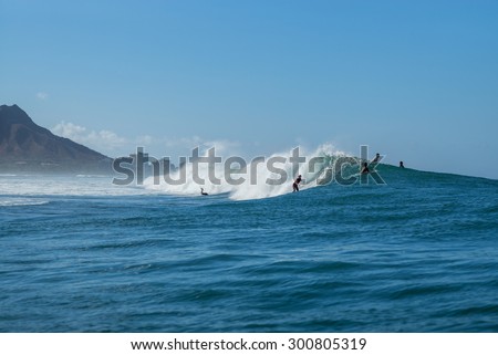 Honolulu, Hawaii, USA, July 28, 2015:  Female surfer clad in a helmet is getting a great ride at Waikiki\'s Ala Moana Bowls Break as a male surfer attempts to dive beneath the breaking wave.