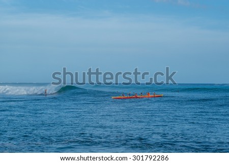 Honolulu, Hawaii, USA, July 31, 2015: Late evening view of an outrigger canoe crew enjoying large surf haze, and wind to assist their paddle home.  Outrigger canoeing is becoming increasingly popular.
