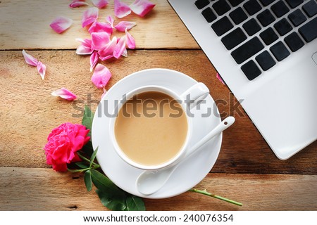 A cup of coffee on wooden table with rose and computer
