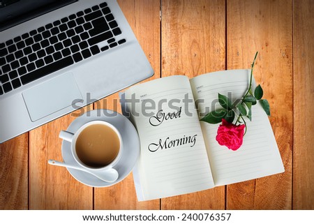 A cup of coffee on wooden table with rose and computer