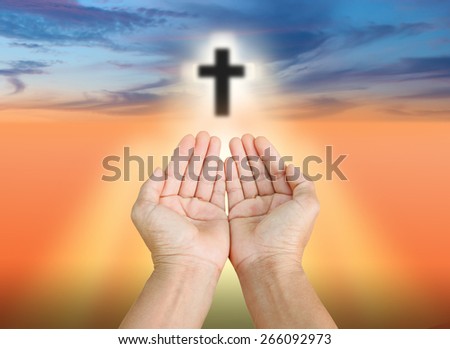 Hands of man praying and the blurred cross on a sunset.