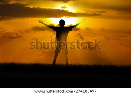 boy standing arms out stretched at sunset.