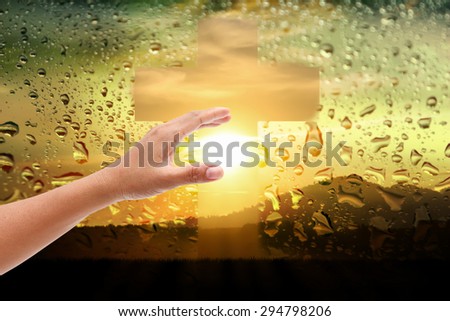 women hand touch the cross and pray at  water drops on sunset mirror background.