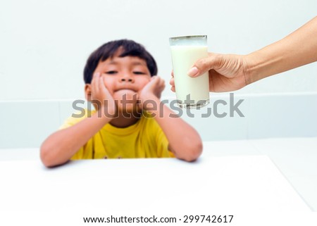 Mother hand holding a glass of milk for a little boy, who do not want to drink milk from glass.