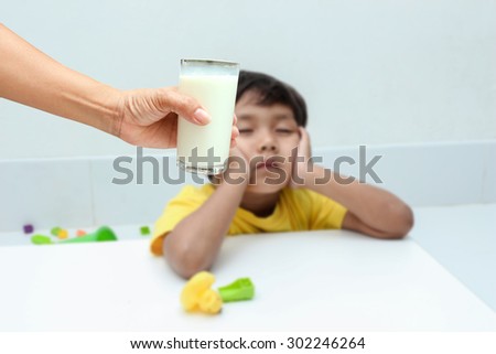 Hand of mother give milk for little boy, who do not want to drink milk from glass.