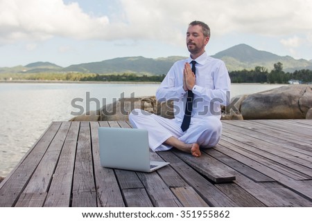 businessman doing yoga on a wooden bridge with a laptop