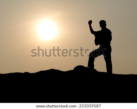 MAN ON TOP OF A MOUNTAIN WITH ONE FIST IN THE AIR