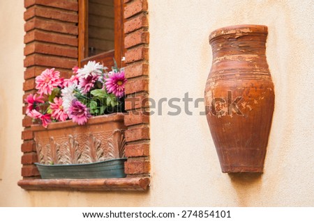 Rustic red brick window with a flowered vase and a terracotta jar set into the wall of a house in Castelmola, Sicily