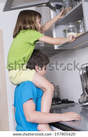 naughty children, one above the other, taking candy from a high kitchen cabinet