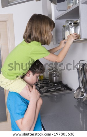 naughty children, one above the other, taking candy from a high kitchen cabinet