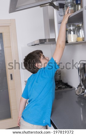 naughty young boy taking candy from a high kitchen cabinet
