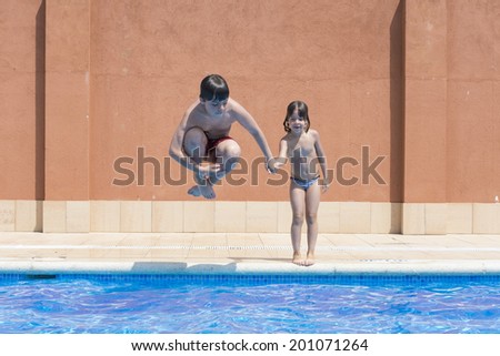a young boy jumping in pump in an outdoor pool while her sister jumps not making a joke