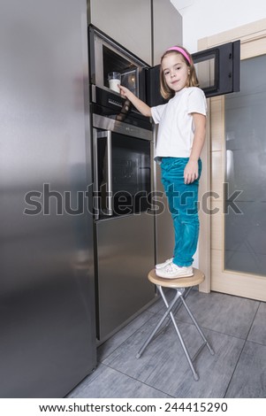 Little girl warming a glass of milk in the microwave