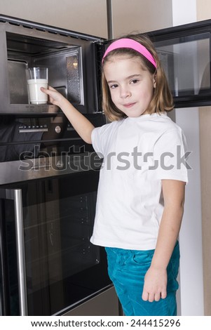 Little girl warming a glass of milk in the microwave