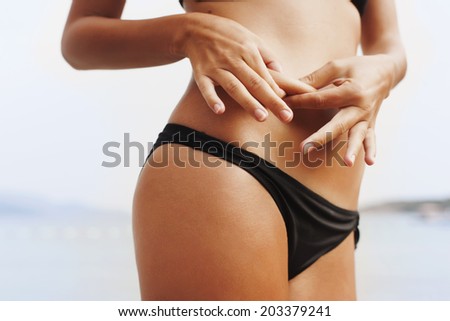 Stomach fat, woman holding skin fat, fit woman on the beach