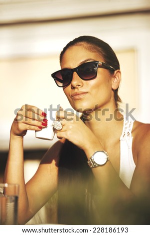 Young pretty woman with pony tail, sunglasses and wrist watch, drinking coffee in a cafe, outdoors