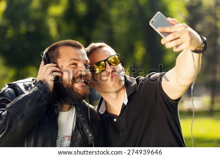 Two friends taking a selfie photo with mobile smart phone in nature, listening to music with headphones
