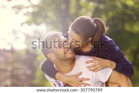 Happy young adult couple outdoors kissing and smiling, she holding on his back