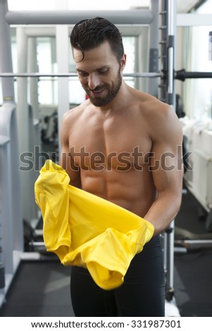Young strong fit man in gym putting t shirt on